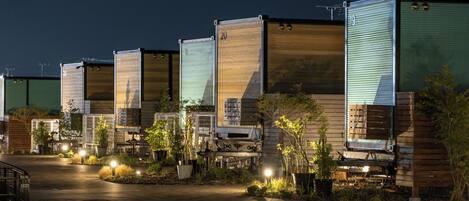 A row of modular cabins with numbered doors, a paved driveway, and outdoor lighting.