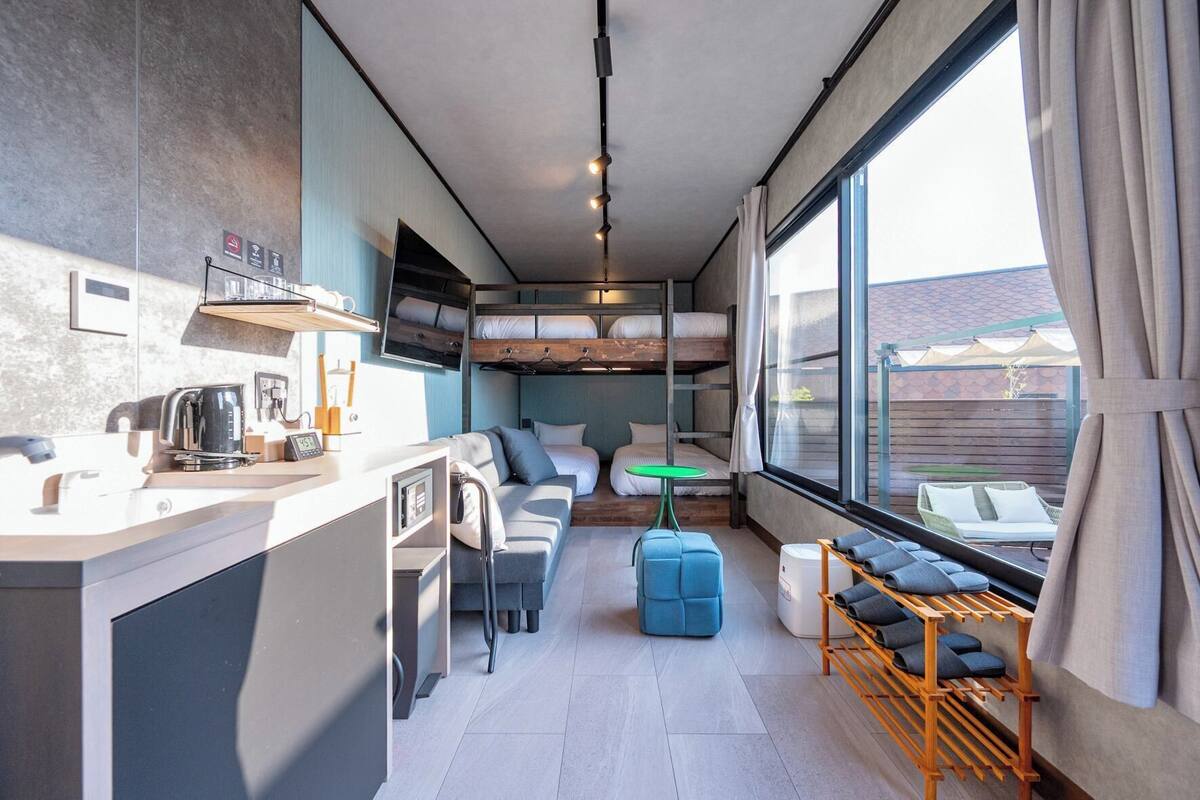 Habitación compacta y moderna con literas, kitchenette, sofá y vistas amplias por grandes ventanales.