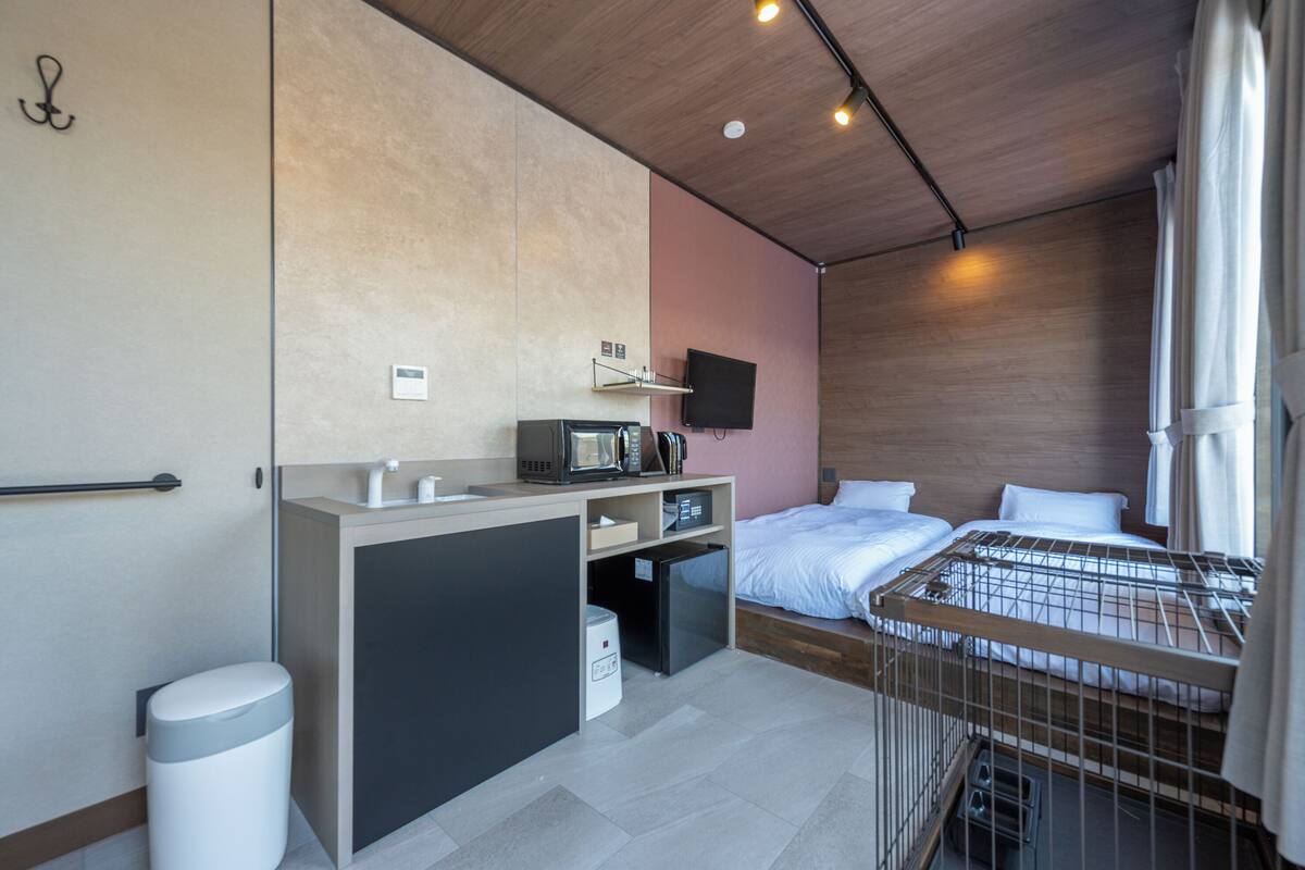 Habitación de hotel pequeña con kitchenette, cama, televisor y vista al exterior.