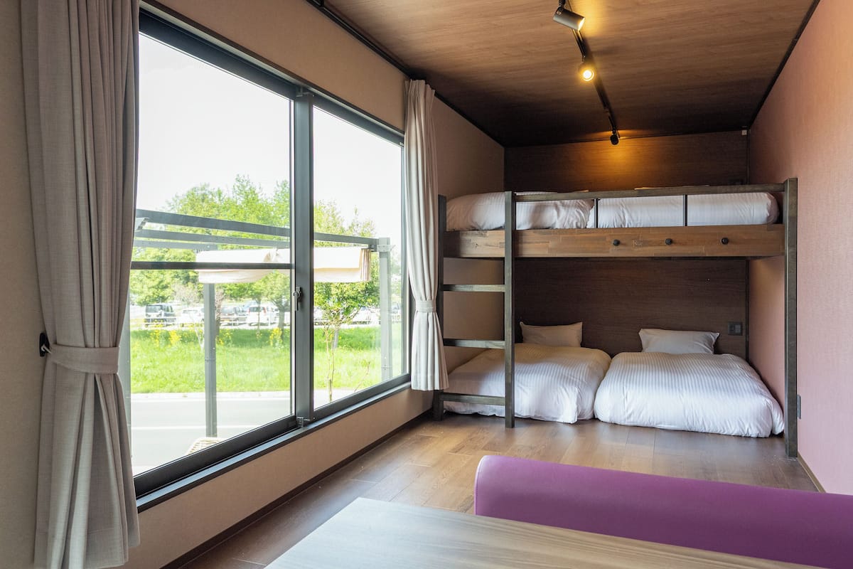 Habitación con literas, un ventanal grande, techo de madera y un banco morado.