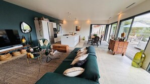 A modern living room with a green sofa, a TV, and a kitchen in the background.