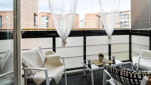 A balcony with white chairs, a small table with a plant, and a view of buildings in the background. - Kotimaailma KotikolmioKauppak saunalla (Lahti)