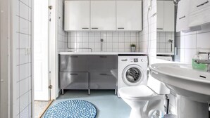 A modern kitchen with white cabinets, a built-in washing machine, a sink, and a round blue rug. - Kotimaailma KotikolmioKauppak saunalla (Lahti)