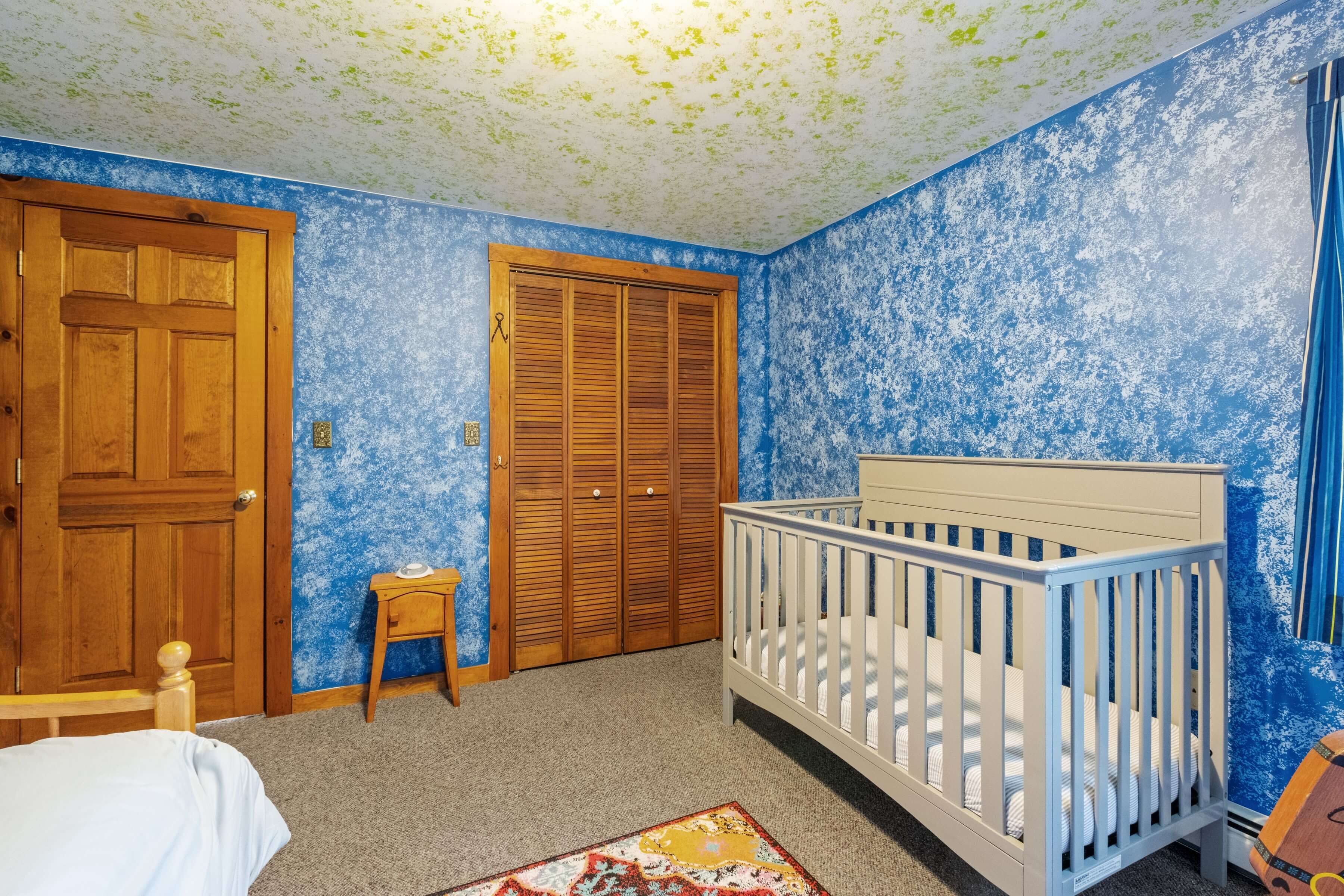 A bedroom with a crib, a wooden door, a closet, and a small table.