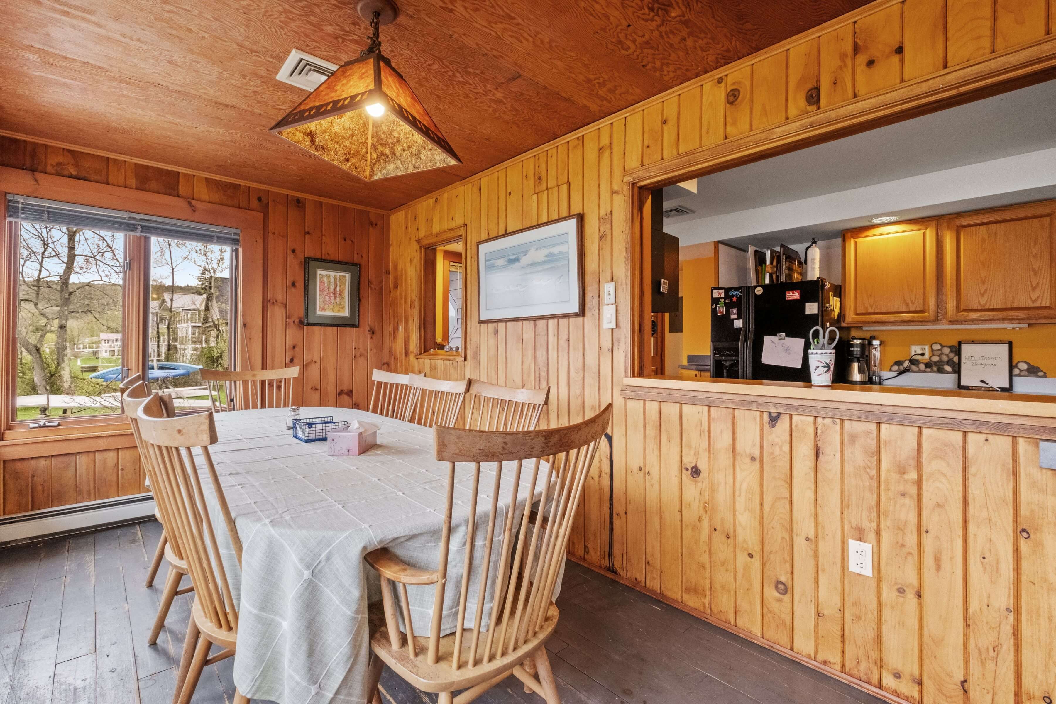 Un interior de madera con una mesa de comedor y sillas, una zona de cocina con electrodomésticos, y vistas por una ventana.