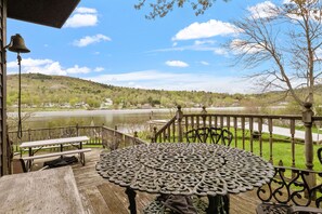 Eine Holzterrasse mit einem Metalltisch und Bänken, mit Blick auf einen See und H ügel.