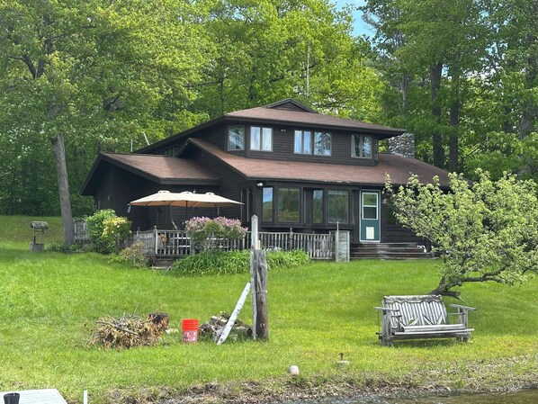 Eine zweistöckige Holzhütte mit Veranda, umgeben von üppiger Vegetation und Bäumen.