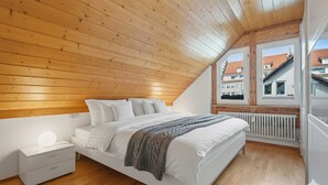 A bedroom with a sloped ceiling, a bed, a nightstand, and a window with a view of buildings. - LAKE Loft Marina (Überlingen)