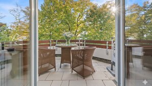 A balcony with wicker furniture, a glass table, and a vase with flowers. - LAKE Loft Marina (Überlingen)