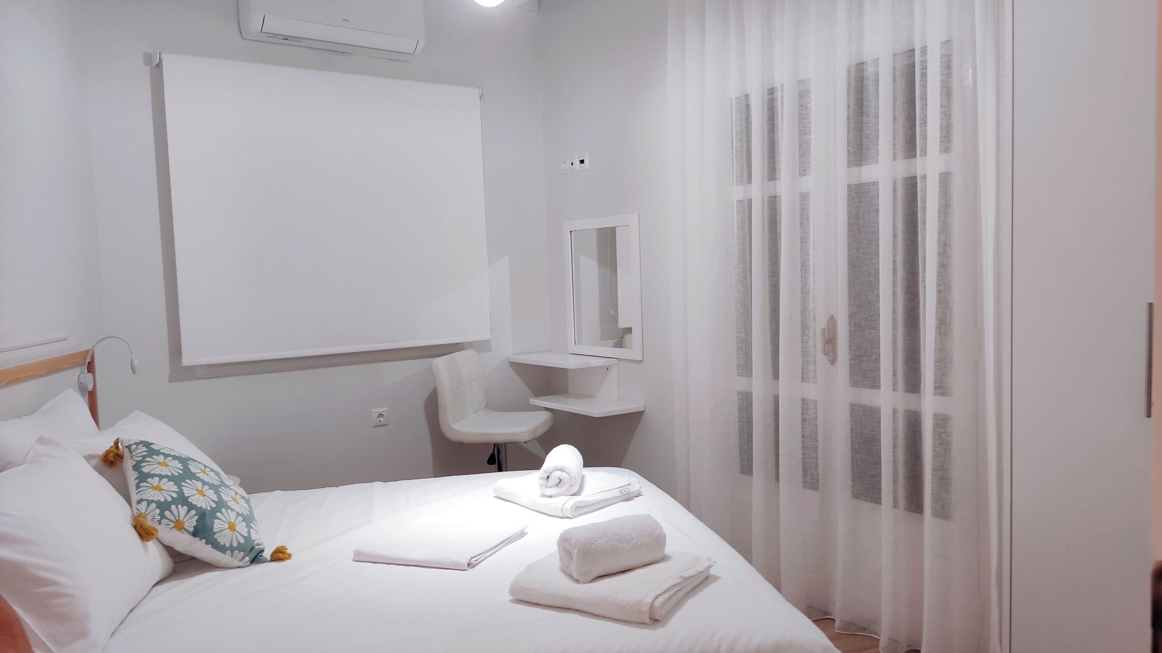 Une chambre d’hôtel avec un lit, une table de chevet, un miroir et une fenêtre avec des rideaux légers.