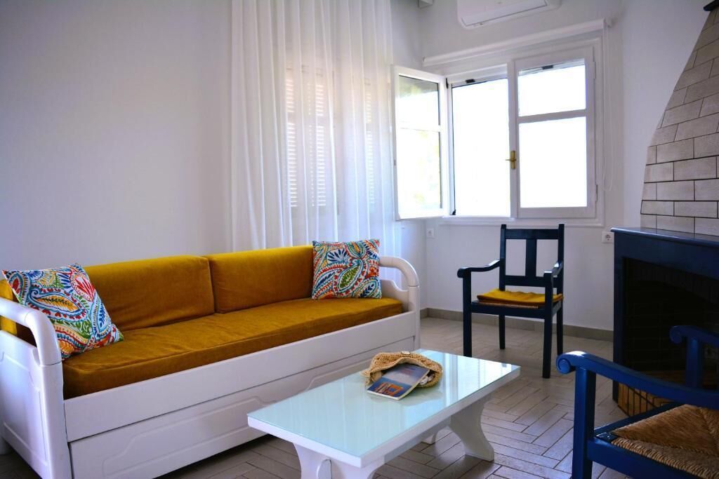 A living room with a mustard-colored sofa, a white coffee table, a blue chair, and a fireplace.