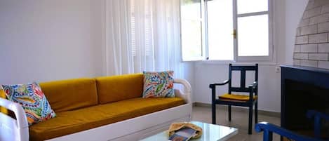A living room with a mustard-colored sofa, a white coffee table, a blue chair, and a fireplace.