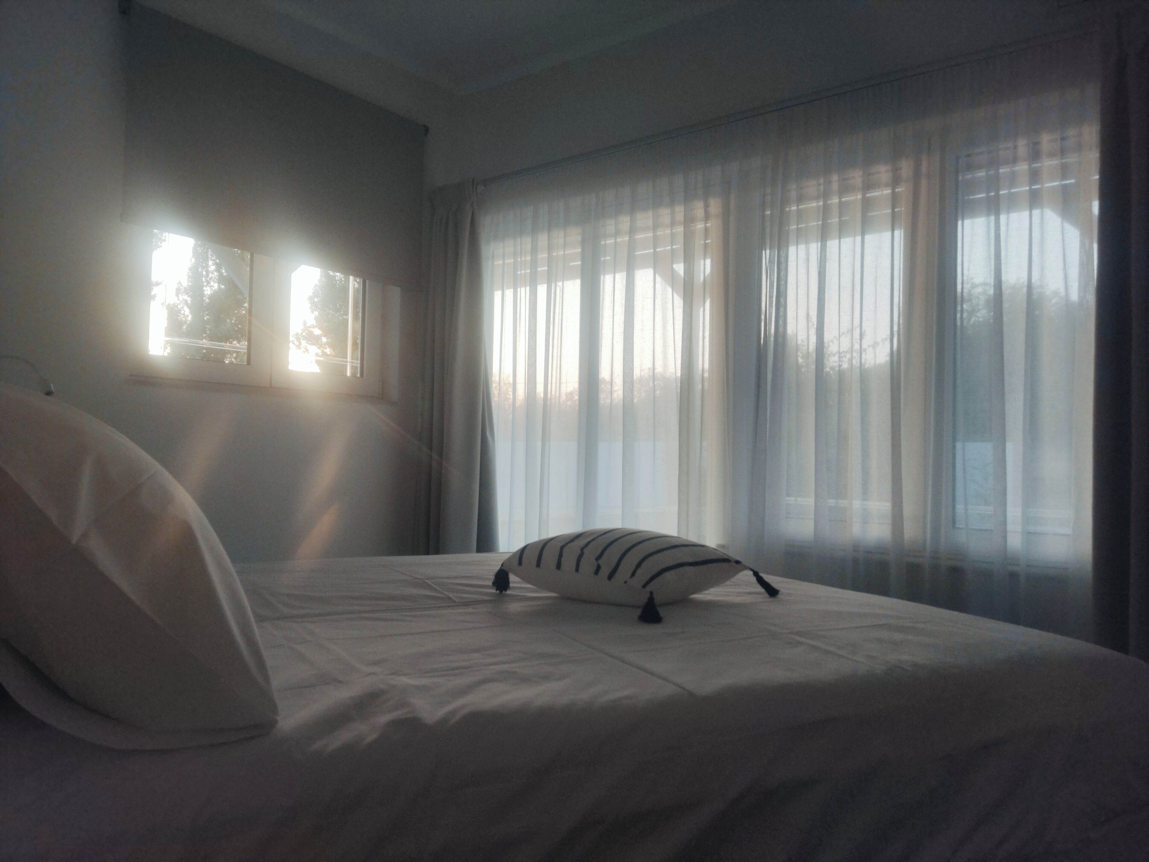 Ein Schlafzimmer mit Bett, Kissen und durchsichtigen Vorhängen.