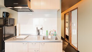 A modern kitchen with a stainless steel sink, a microwave, and wooden cabinets. - CU Host Dotonbori No.1 Mansion (Osaka)