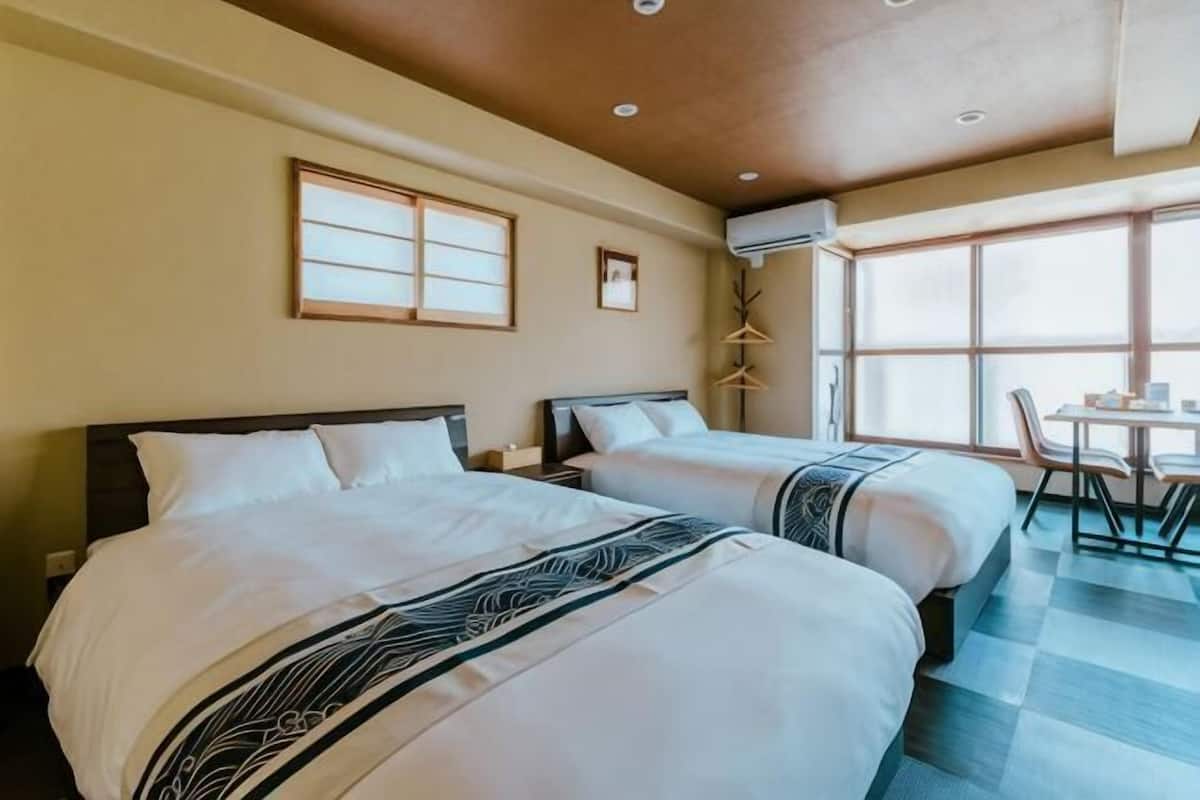 Quarto de hotel com duas camas, área de refeições e uma janela grande.