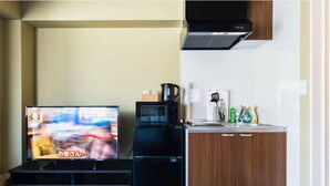 Ein kompakter Wohnraum mit Fernseher, Kaffeemaschine, Mikrowelle und einer kleinen Küchenzeile mit Schränken und Spüle.
