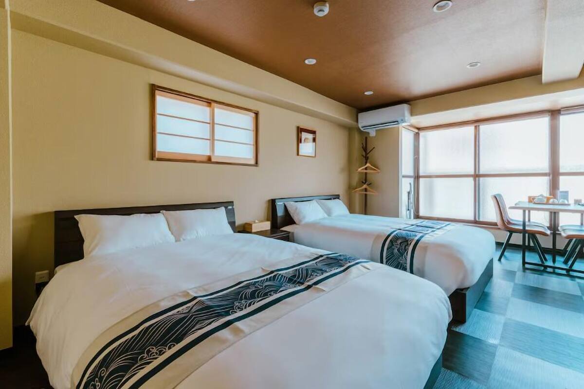 Quarto de hotel com duas camas, uma mesa de jantar e uma janela com vista.