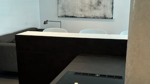 Een moderne kantoorruimte met een wit bureau, een zwarte scheidingswand, een potplant en een groot abstract schilderij aan de muur.
