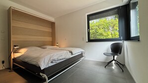 Een moderne slaapkamer met een bed, nachtlampjes, een raam met zonwering en een stoel.