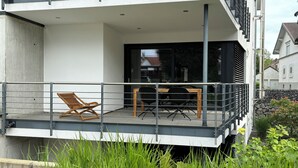 Een balkon met een houten stoel, een tafel en een glazen deur die naar de binnenruimte leidt.