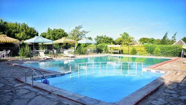 A rectangular swimming pool with a stone border, surrounded by lounge chairs and umbrellas. - Elboran Resort and spa (Isiolo)