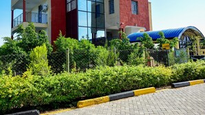 A multi-story building with a red and beige facade, large glass windows, and a blue roof structure. - Elboran Resort and spa (Isiolo)