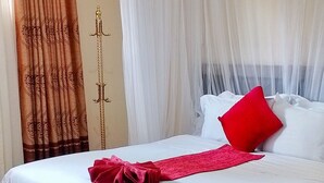 A hotel room with a bed, white curtains, a red pillow, and a decorative curtain with a tree pattern. - Elboran Resort and spa (Isiolo)