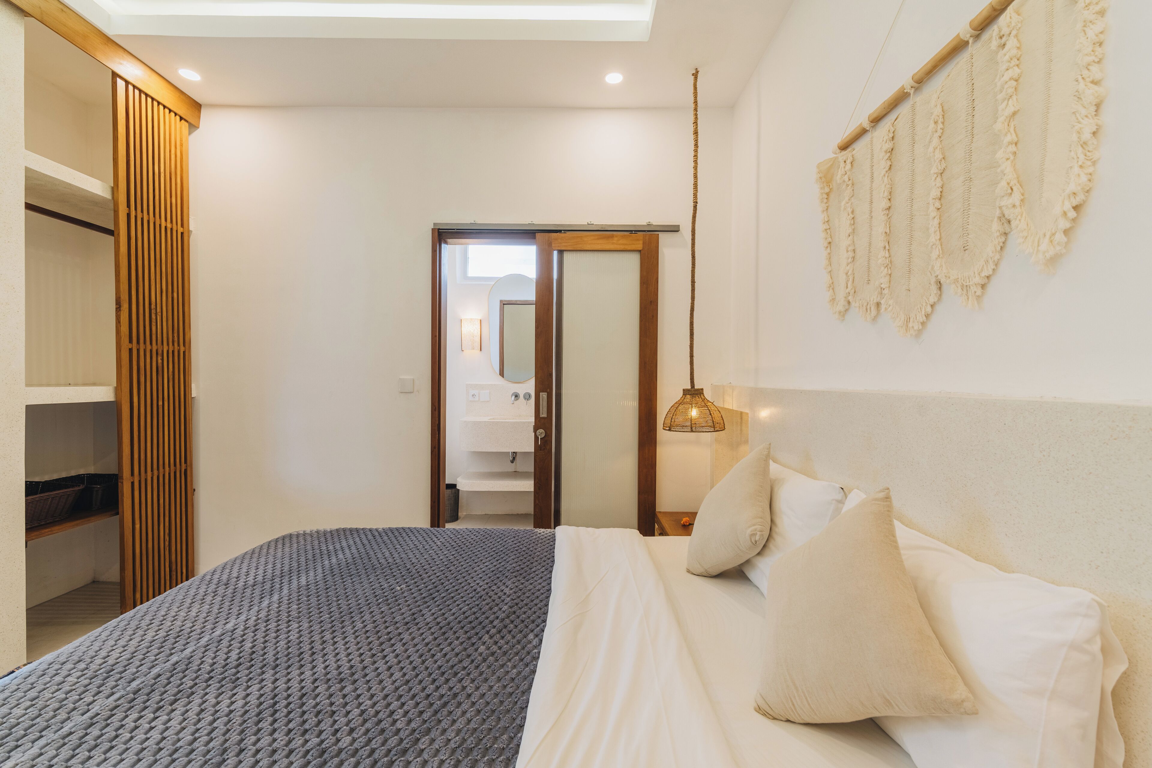Een slaapkamer met een bed, kussens, een nachtkastje, een hanglamp en een garderobe.