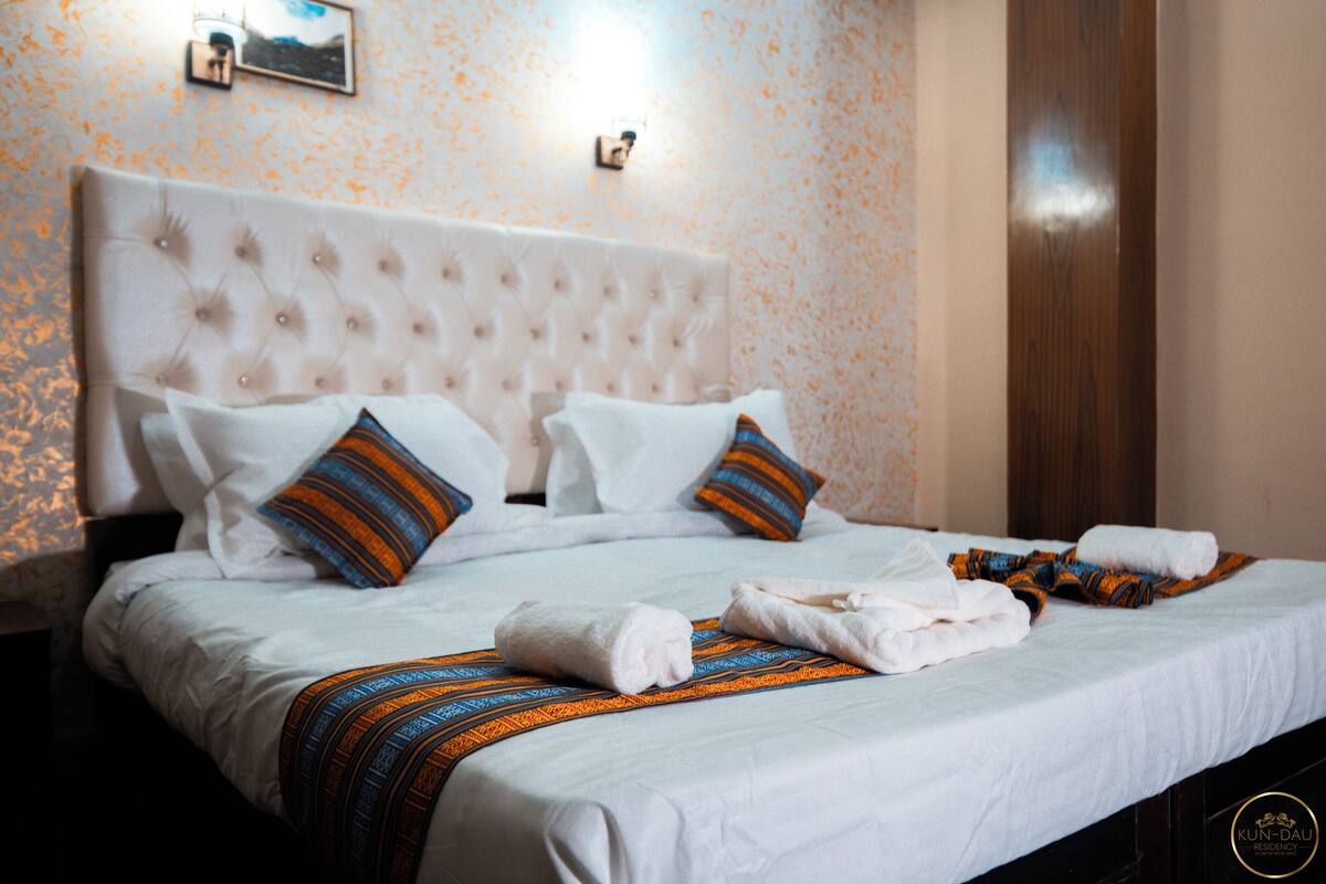 Una cama bien hecha con sábanas blancas, almohadas a rayas y una manta decorativa.