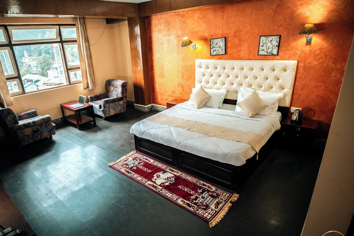 Un dormitorio con una cama grande, una silla, una mesita y una ventana.