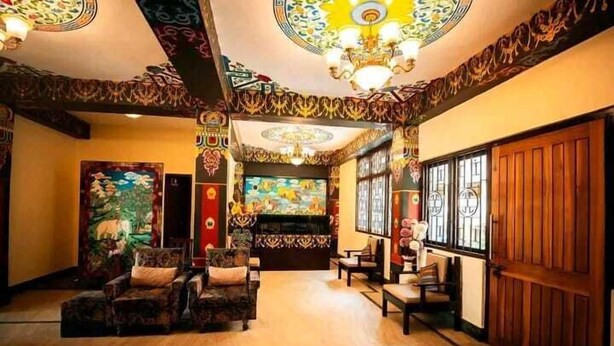 A room with a wooden floor, patterned walls, and a large mural. There are two sofas and a table in the center. - Kun Dau Residency (Gangtok)