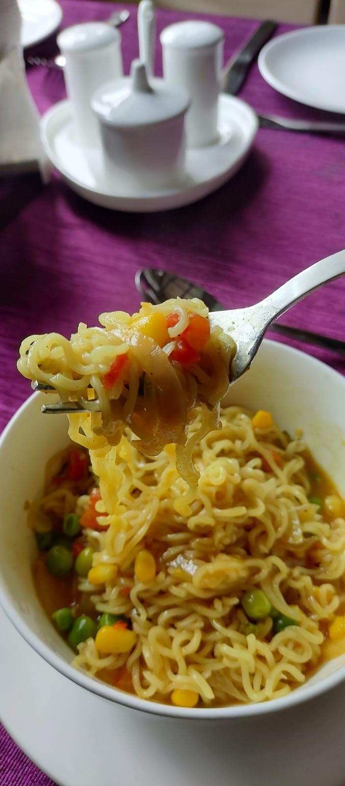 A bowl of noodles with vegetables being lifted with a fork.