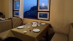 A dining area with a table set for two, a large window with multiple panes, and a view of a cityscape at dusk. - Kun Dau Residency (Gangtok)