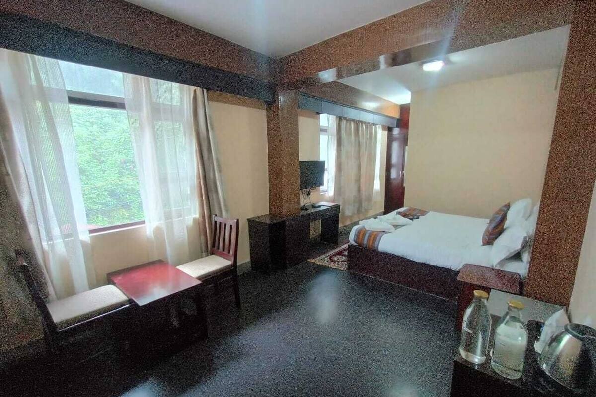 Una habitación de hotel con cama, escritorio, silla y ventana con cortinas.