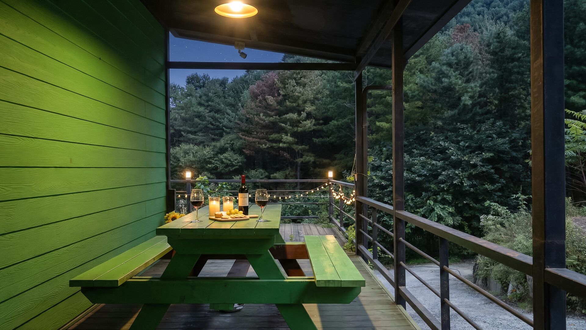 Um deck de madeira verde com uma mesa de piquenique, velas e luzes de cordão.