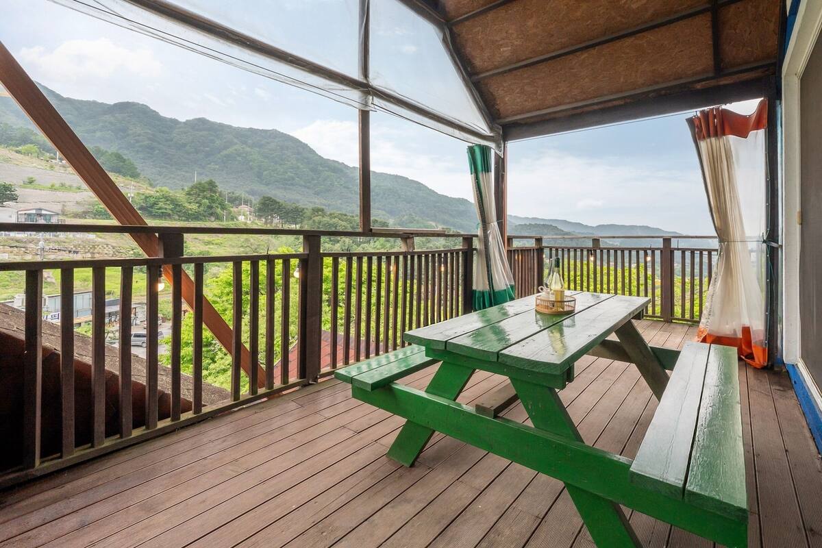 Une terrasse en bois avec une table de pique-nique et une bouteille de vin, offrant une vue sur un paysage montagneux.