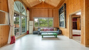Una habitación amplia con paredes de madera y un techo alto, que cuenta con un ventanal grande, un conjunto de sofás y una mesa de centro verde.