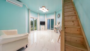 Amplia habitación con sofá de cuero blanco, escalera de madera y un ventanal con vistas a la vegetación.