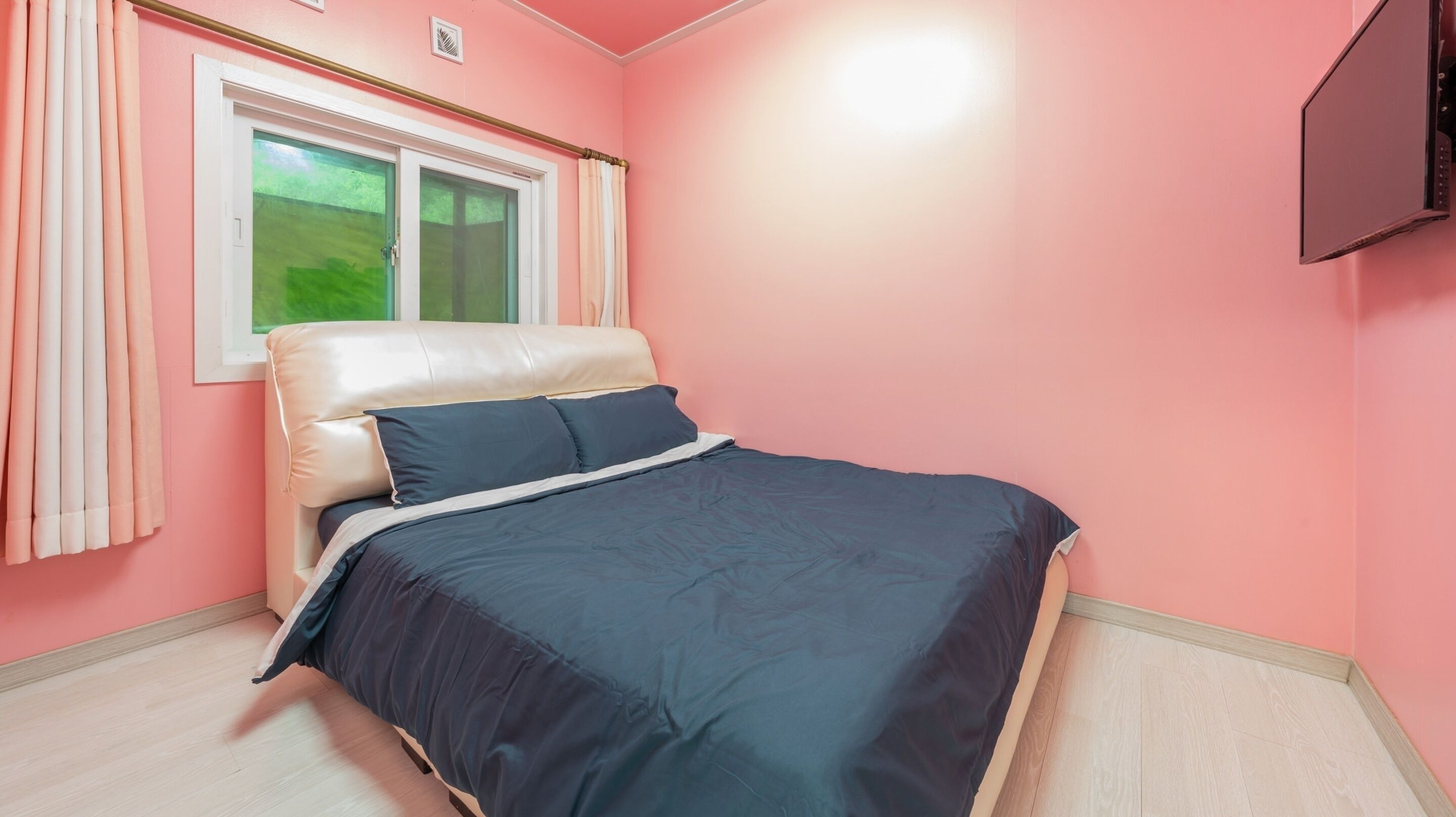 A bedroom with a bed, curtains, a window, and a TV mounted on the wall.