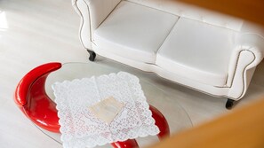Un canapé en cuir blanc orné d’une bordure décorative et une chaise rouge avec un chemin de table en dentelle et un livre.