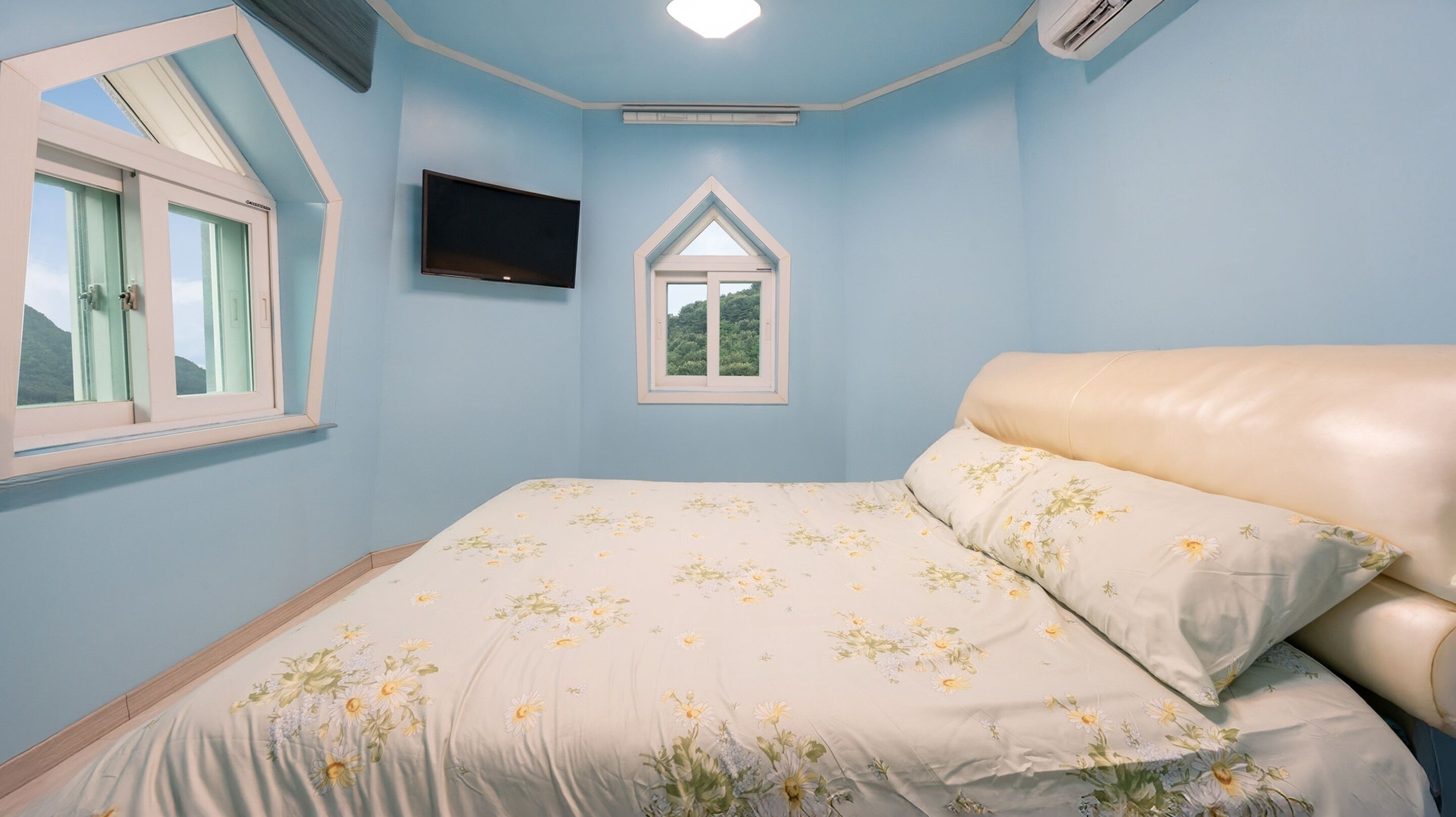 A bedroom with a bed, a TV, a window, and an air conditioning unit.