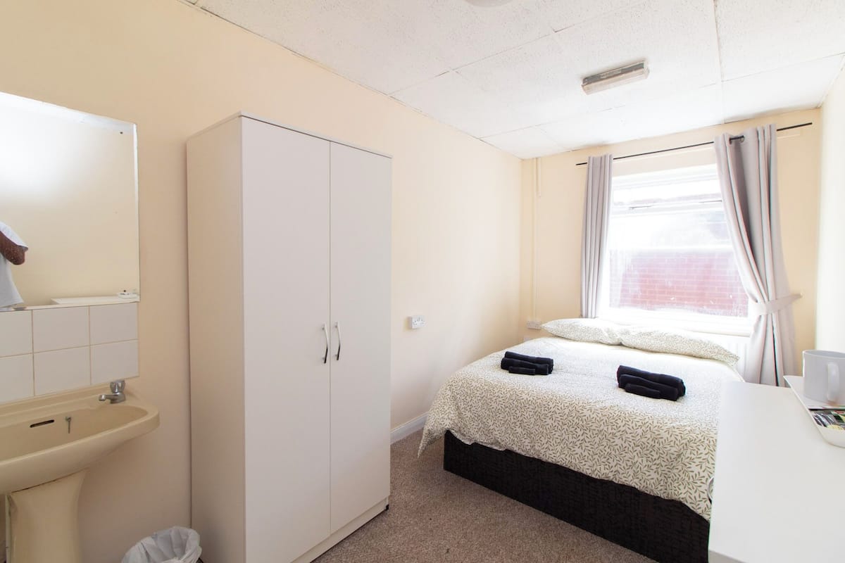 Ein Hotelzimmer mit einem Bett, einem Kleiderschrank, einem Waschbecken und einem Fenster mit Vorhängen.
