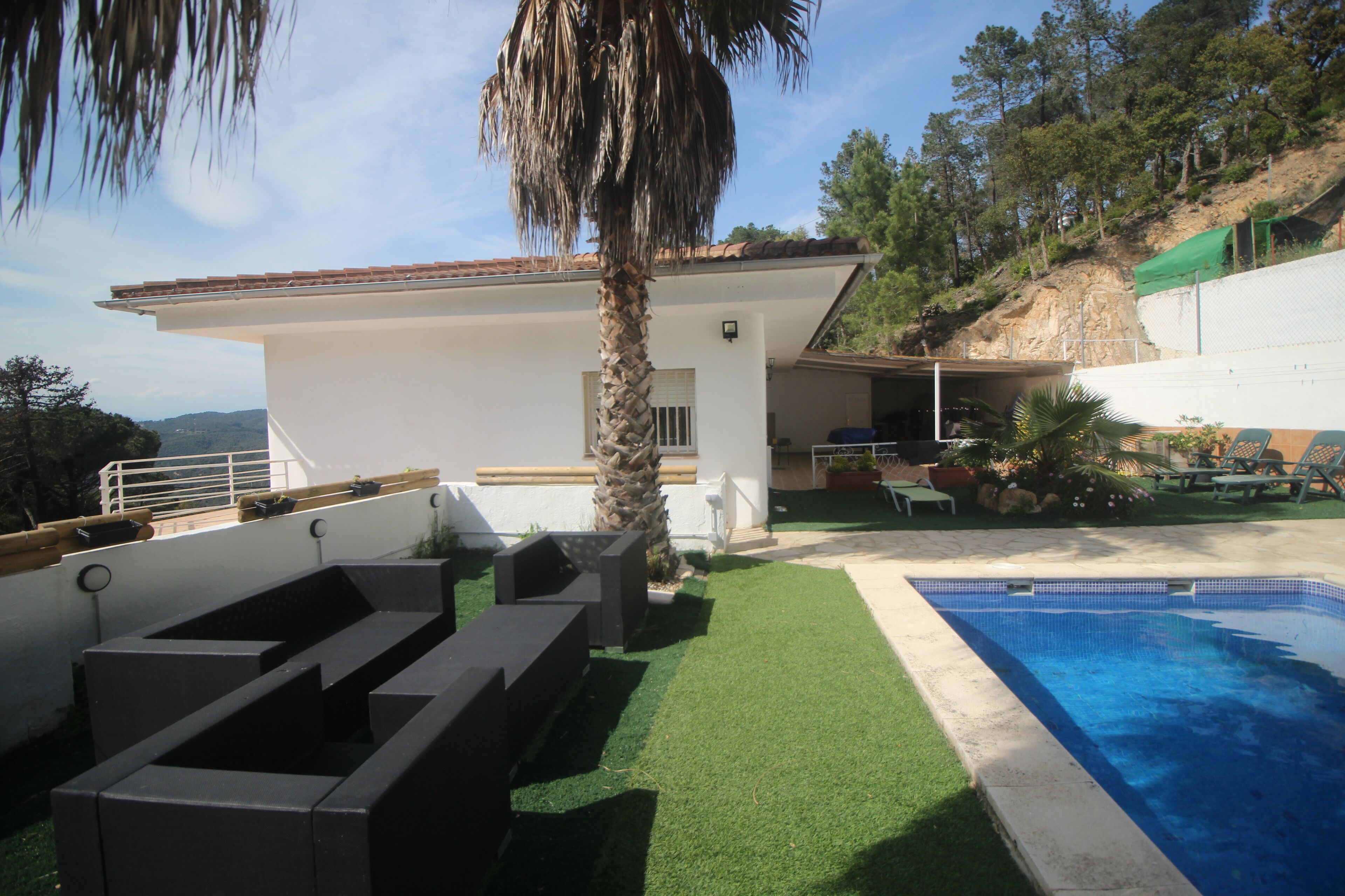 Una casa moderna amb piscina, un patí amb mobles d'exterior i vista del paisatge circumdant.