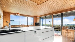 Une cuisine moderne dotée d’un grand îlot central, d’un plafond en bois et de grandes fenêtres offrant une vue sur le paysage.