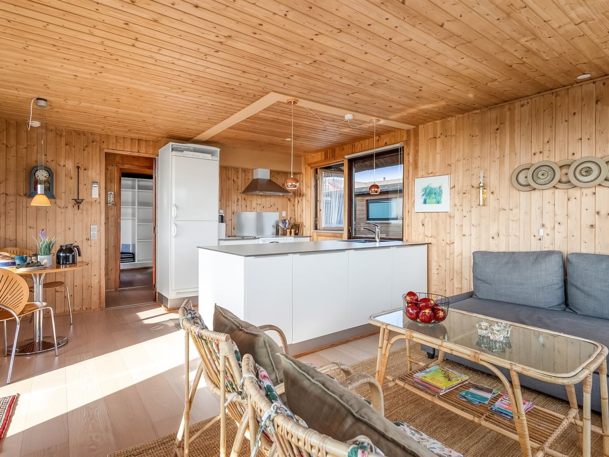 Un intérieur de chalet chaleureux avec un plafond en bois, un coin cuisine, un espace repas et un salon comprenant un canapé et une table basse.