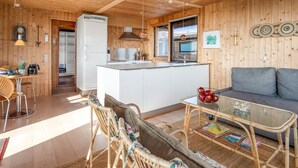 Un intérieur de chalet chaleureux avec un plafond en bois, un coin cuisine, un espace repas et un salon comprenant un canapé et une table basse.