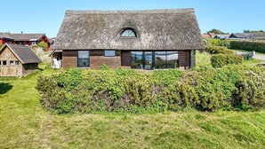 Une maison moderne avec un toit de chaume, de grandes fenêtres et un jardin bien entretenu.