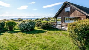 Une maison en bois dotée d’un balcon en verre donnant sur une zone herbeuse et un plan d’eau.