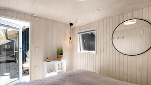 Un dormitorio con una cama grande, un espejo redondo, una ventana y un armario blanco con una planta.