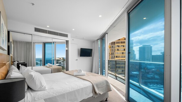 A modern hotel room with a large bed, a flat-screen TV, and a balcony with a city view.